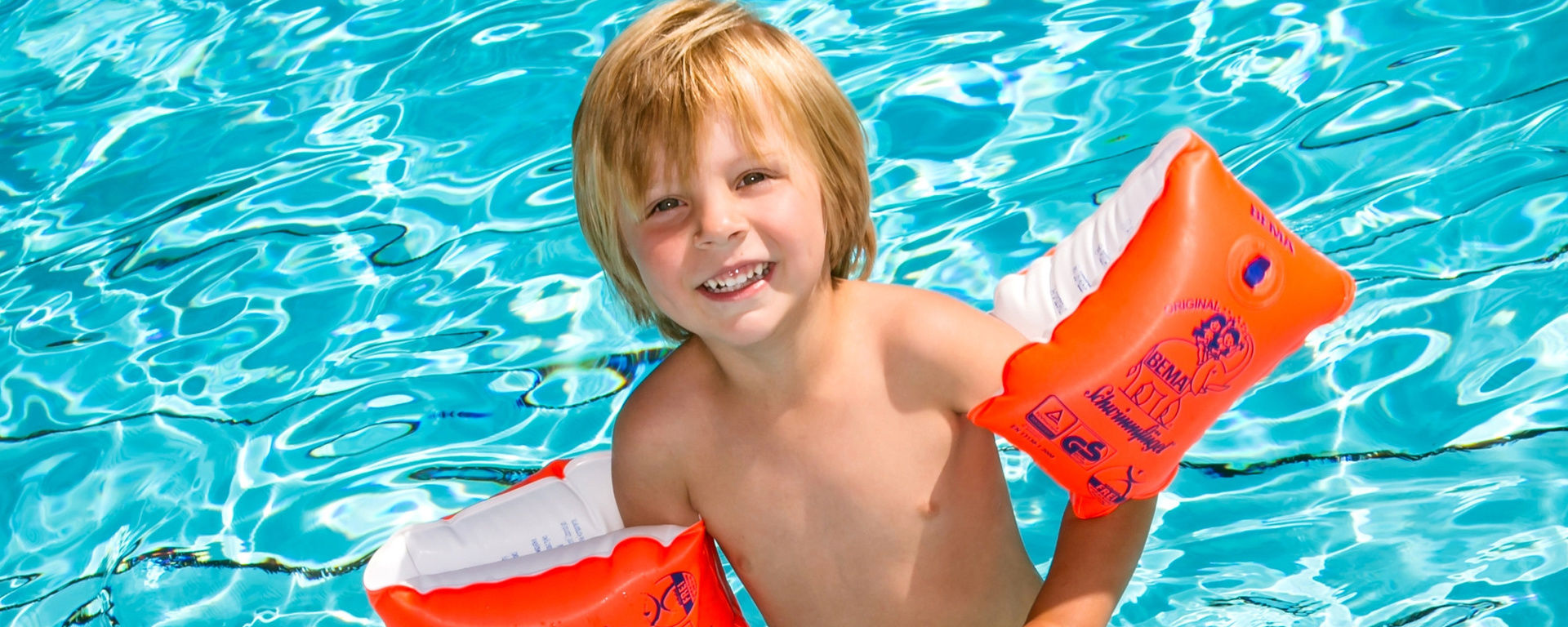 Junge grinst mit Schwimmflügel aus dem Wasser