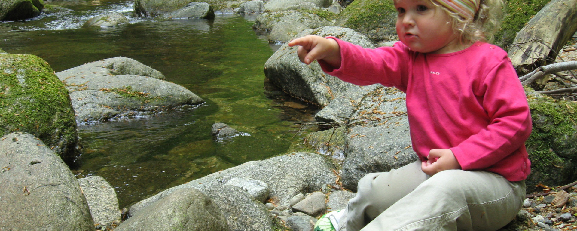 Kleines Mädchen beim Wandern zeigt auf große Steine, die sie entdeckt hat