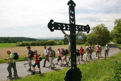 Wanderer jeden Alters durch Freyung bei Sonnenschein neben weiten Feldern und grüner Landschaft