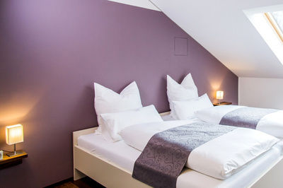 Modernes Bett mit weißer Bettwäsche vor einer lila Wand