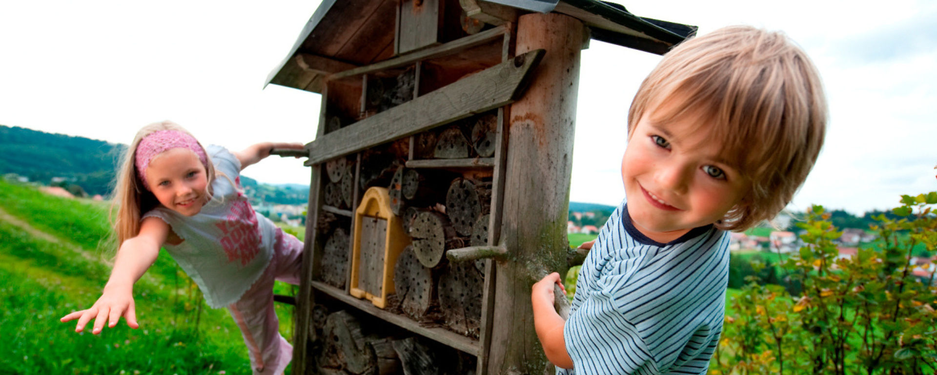 Kinder freuen sich über ein Insektenhotel auf einer Wiese