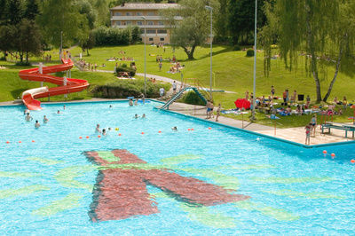 Panorama über das Freibad mit vielen Kindern, die Spaß im Wasser und auf der Rutsche haben