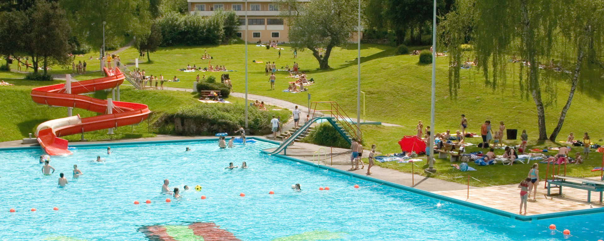 Panorama über das Freibad mit vielen Kindern, die Spaß im Wasser und auf der Rutsche haben