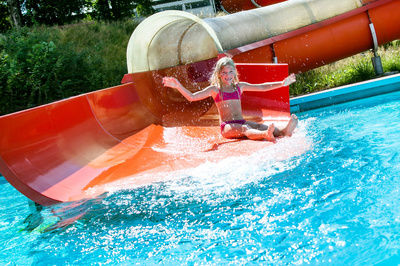 Mädchen rutscht lachend eine Wasserrutsche runter in ein großes Wasserbecken