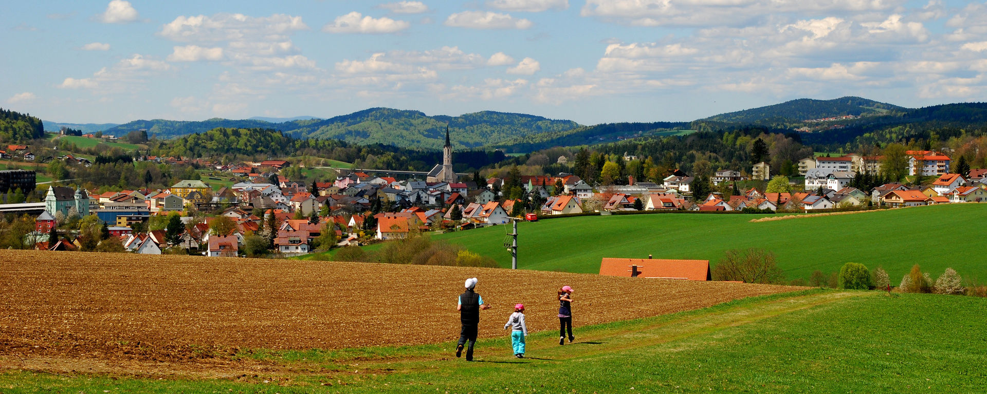 Kinder laufen spielend über eine große Wiese neben einem Feld und genießen die Sonnenstrahlen