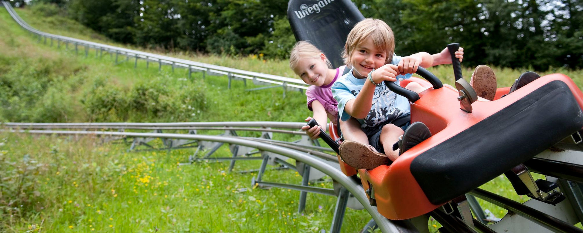 Geschwister lachen beim Rodeln mit einem Bob im Sommer