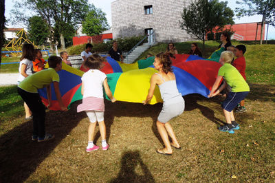 Kinder spielen mit einem großen Tuch und halten dies alle gemeinsam in die Luft