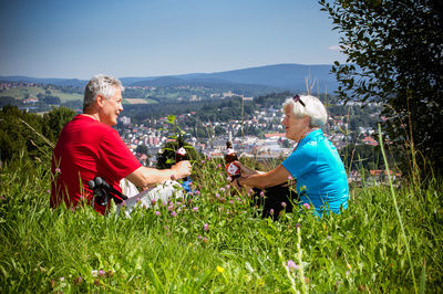 Zwei Wanderer machen Pause in einer grünen, großen Wiese mit Blick auf die Stadt