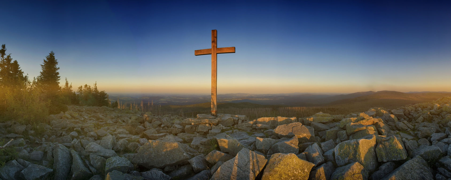 Gipfelkreuz am Lusen auf großen Steinen vor einer malerischen Aussicht in die Weite des Bayerischen Waldes